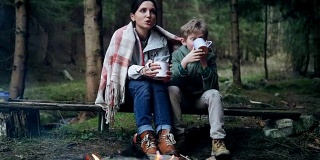 母亲和儿子在森林篝火旁唱歌喝茶