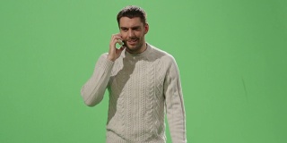 一个随意的白人男子正在一边走一边讲电话，背景是一个绿色的模拟屏幕。
