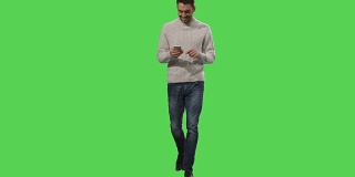 一个随意的白人正在走路，在绿色屏幕上使用智能手机。