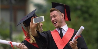 戴着学位帽和学士服在智能手机上拍摄视频的快乐男女