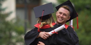 毕业典礼后年轻的毕业生拥抱着，美丽的人们微笑着