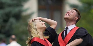 毕业晚会上，笑嘻嘻的情侣谈笑风生，男人把帽子抛向空中，幸福无比