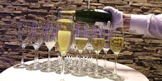 侍者把香槟倒进玻璃杯里，香槟玻璃杯放在自助餐桌上，室内，特写