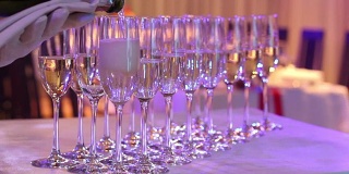 侍者将香槟倒入玻璃杯中，香槟玻璃杯放在自助餐桌上，餐厅或酒店的大厅里，侍者的手上戴着白手套拿着一瓶香槟，室内，特写