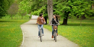 两个女性朋友在公园里骑自行车。年轻有趣的女人与自行车花时间在一起