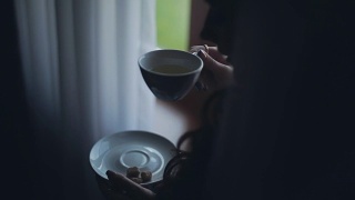近景黑发女人看向远处和饮茶。早上一个人在家的女性视频素材模板下载