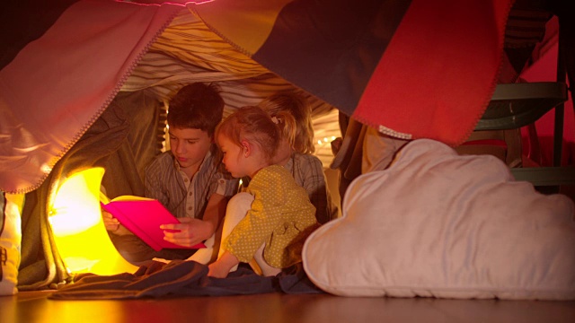 小孩子们在他们的毛毯堡垒里读一个晚上的故事