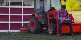 Farmer坐在拖拉机上使用笔记本电脑