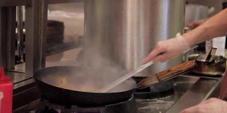 在餐厅的厨房里，一名男子在热煎锅上搅拌蔬菜和肉