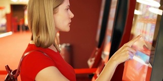 穿着红t恤的年轻漂亮女人在电影院的自动贩卖机里买电影票