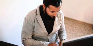一个留着胡子，穿着夹克在电脑前工作的人
