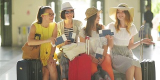 微笑的女性朋友很高兴一起去度暑假。四个女孩拿着护照和机票在机场候机