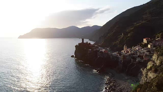 旅游地标Vernazza的鸟瞰图。Vernazza是一个地中海小镇，位于利古里亚的Cinque terre国家公园。日落有云和耀斑。4k无人机侧面视频拍摄