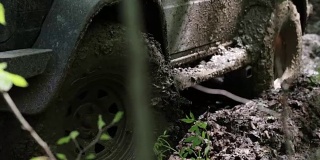 一辆黑色越野车陷在了森林里的泥里