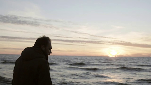 一个年轻人独自走在海边，看着海浪。男人们在海滩上欣赏日落