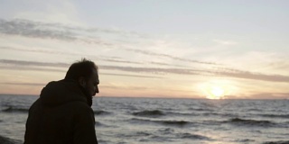 一个年轻人独自走在海边，看着海浪。男人们在海滩上欣赏日落