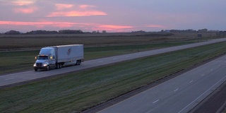 特写:在玫瑰色的夕阳下，半挂车行驶在空旷的乡村道路上