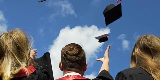快乐的年轻人庆祝毕业，把学术帽抛向空中