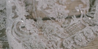 近距离滑动拍摄的细节上的婚纱躺在木制的表面上，美丽的白色婚纱为一个新娘。
