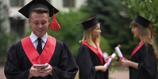 35、男毕业生在手机上打字短信，对着镜头微笑，毕业了