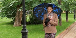 年轻悲伤的女人在雨中漫步在公园里。