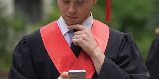 认真的男毕业生一边揉下巴一边看手机，收到了好消息