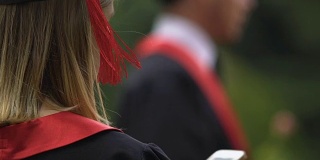 近距离的女研究生在学术长袍上阅读智能手机上的信息