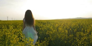 在一个阳光明媚的日子里，穿着白色连衣裙的女孩走过油菜籽田