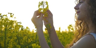 一个乡村女孩优雅地触摸着站在草地上的油菜花的慢镜头