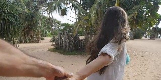 跟着我拍的一个年轻女人拉着她的男朋友在海边。女孩牵着男人的手，在热带异国的海滩上奔向大海。暑假或假期。的观点。观点慢动作