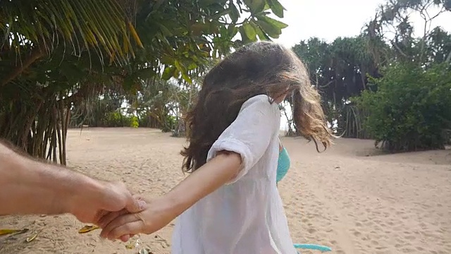 女孩牵着男人的手，在热带异国的海滩上奔向大海。跟着我拍的一个年轻女人拉着她的男朋友在海边。暑假或假期。的观点。观点慢动作