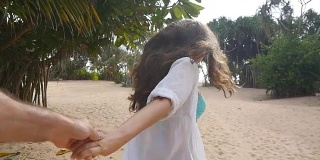 女孩牵着男人的手，在热带异国的海滩上奔向大海。跟着我拍的一个年轻女人拉着她的男朋友在海边。暑假或假期。的观点。观点慢动作