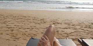 年轻女子躺在海边晒日光浴的床上。女性的腿在躺椅上放松和享受暑假在海洋海滩。一个度假胜地女孩的脚。近距离观点