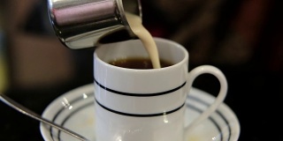女人的手拿着一个小罐子，把牛奶倒进桌上的热茶里并搅拌。