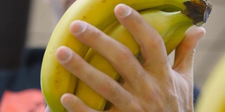 男手在超市挑选香蕉。一个男人从杂货店的柜台上拿着一串香蕉。小伙子正在商店的农产品部挑选新鲜水果。买家选择食物。近距离