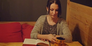 迷人的年轻女子坐在咖啡馆的沙发上看书和喝咖啡