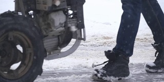 冬天，一个男人用扫雪机清除人行道上的积雪。雪花向四面八方飞去。慢动作