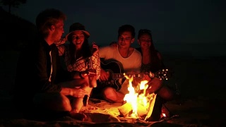 年轻人晚上在海滩上用篝火野餐。欢快的朋友们唱着歌，弹着吉他。Slowmotion拍摄视频素材模板下载