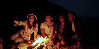 年轻人晚上在海滩上用篝火野餐。愉快的朋友在电话里拍照。Slowmotion拍摄