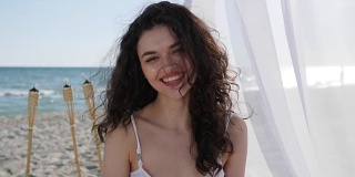 肖像美丽的女孩在海滩上，快乐的女人卷着头发，夏天度假的女人在海边，女性美丽的脸微笑