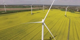 鸟瞰图近距离的风力涡轮机螺旋桨叶片在黄色的油菜田与蓝天。