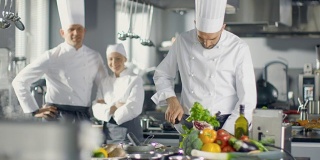 一家大餐厅的著名厨师在现代厨房里双臂交叉微笑。他的员工在背后微笑。