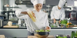 在一家著名的餐厅，女厨师准备沙拉，广告油。她在一家现代化的大厨房工作。