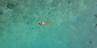 鸟瞰图一个迷人的女人在比基尼漂浮在水晶清澈的海洋。一个美丽的女孩在印度洋游泳