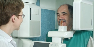 牙科医生在检查前使用全景和头部x光扫描仪与一位老年病人交谈