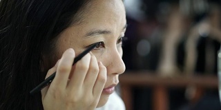 亚洲女人在镜子前化妆，画眼线的慢动作。美容化妆概念