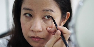 亚洲女人在镜子前化妆，画眼线的慢动作。美容化妆概念