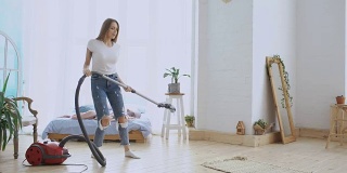 年轻女子有乐趣打扫房子与吸尘器跳舞和唱歌在家里