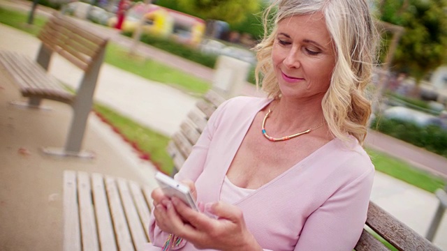 在公园里用智能手机发短信的漂亮老女人