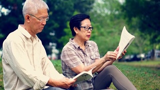 一对亚洲老夫妇在公园看书。花宝贵的时间，永远不要停止学习新东西视频素材模板下载